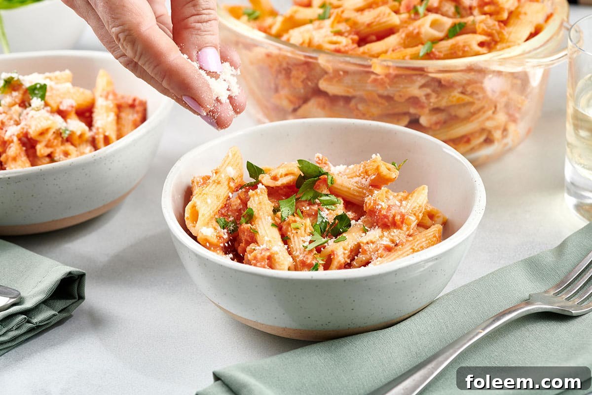 Woman sprinkling parmesan cheese onto a bowl of Penne alla Vodka.
