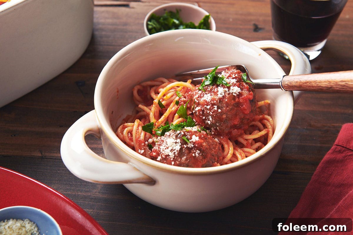 Spaghetti and meatballs with tomato sauce in white bowl on table.