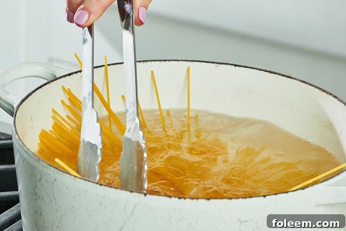 Stirring spaghetti in white pot of boiling water with tongs.