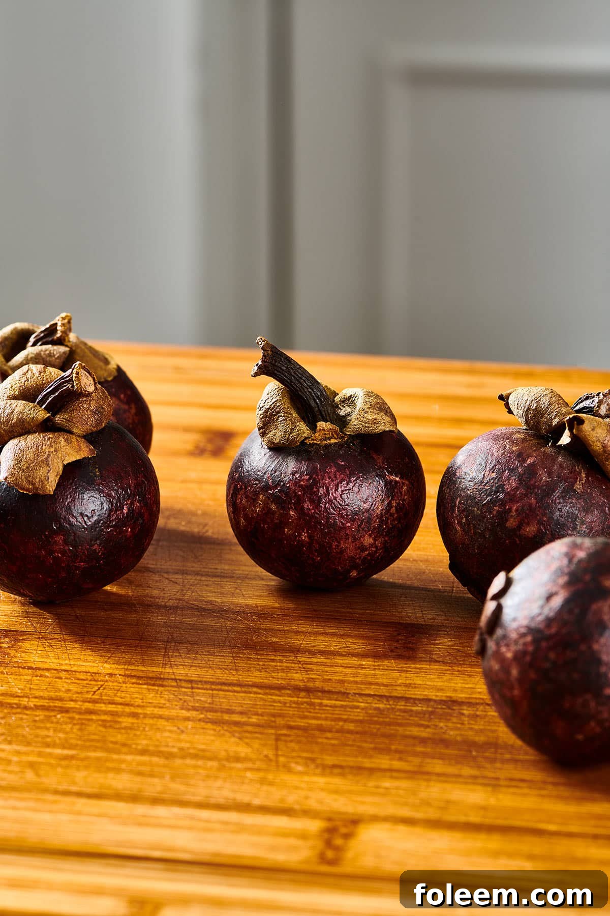 Group of fresh mangosteen fruits on wood cutting board in a kitchen.