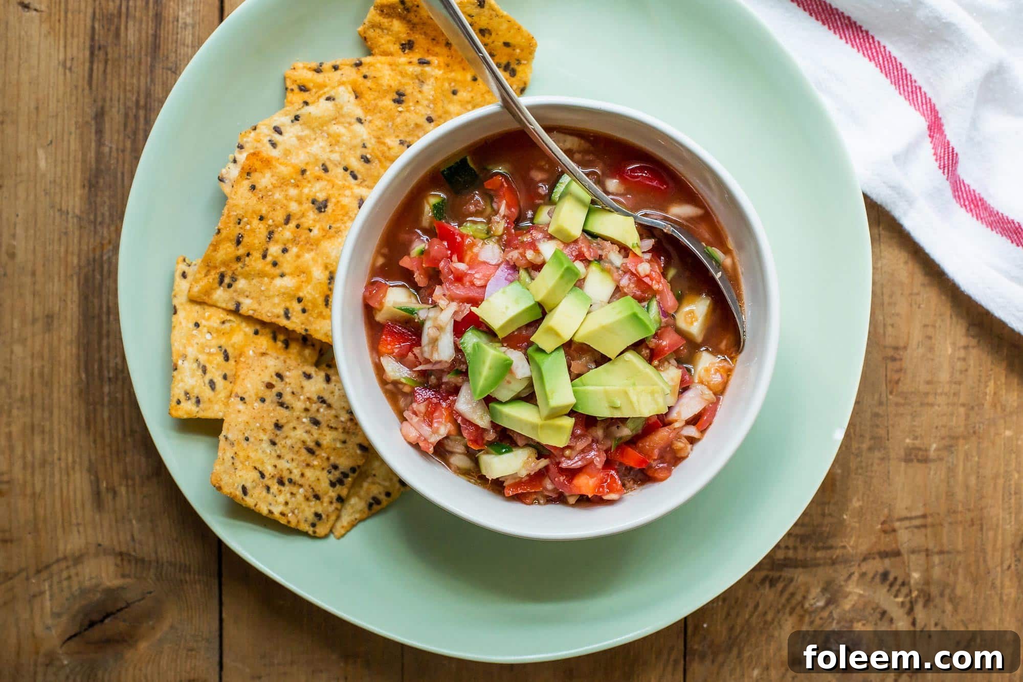 Gazpacho in bowl on plate with chips.