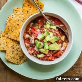 Gazpacho in bowl on plate with chips.