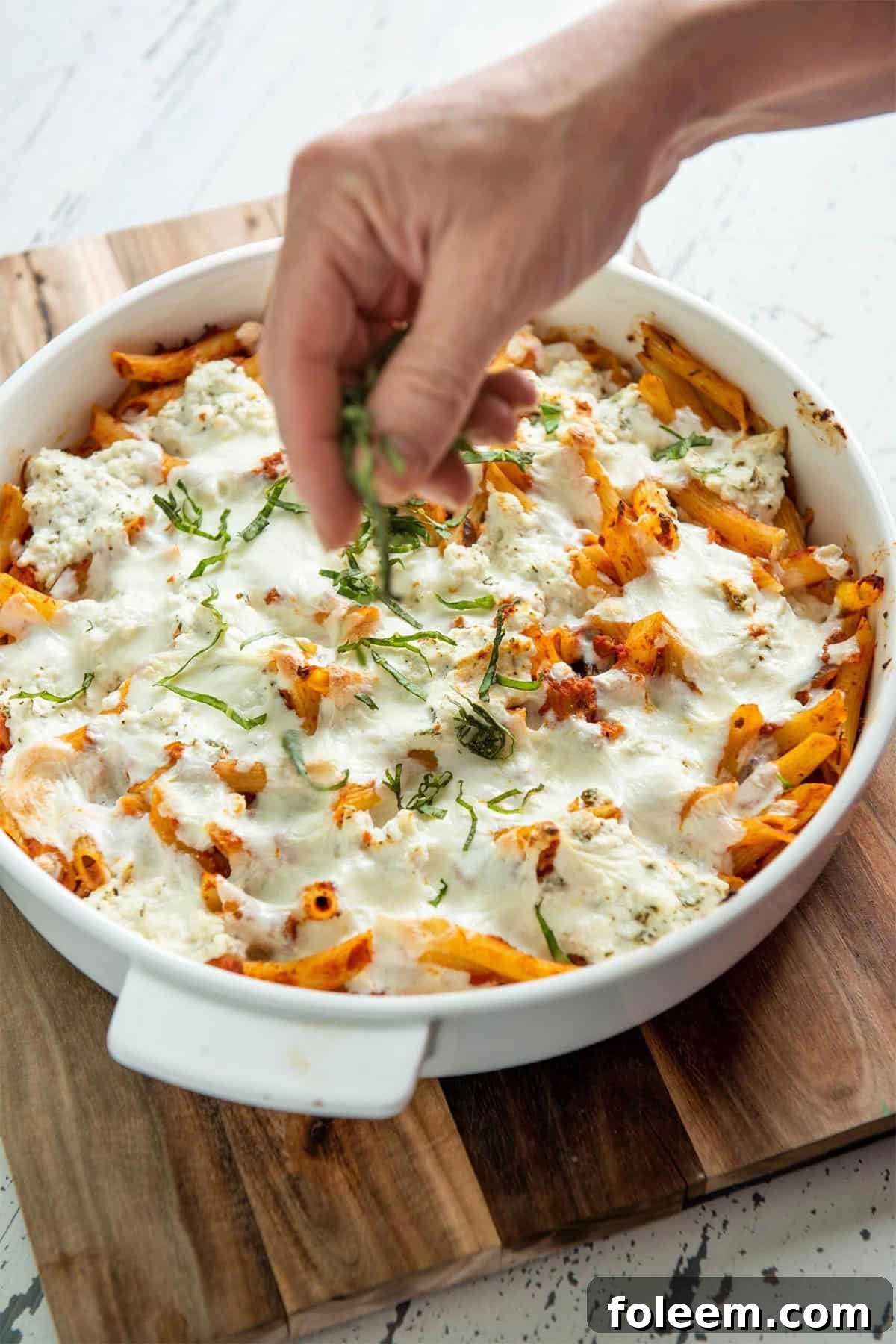 Woman sprinkling thinly-sliced basil onto a dish of Baked Pasta with Bolognese Sauce.