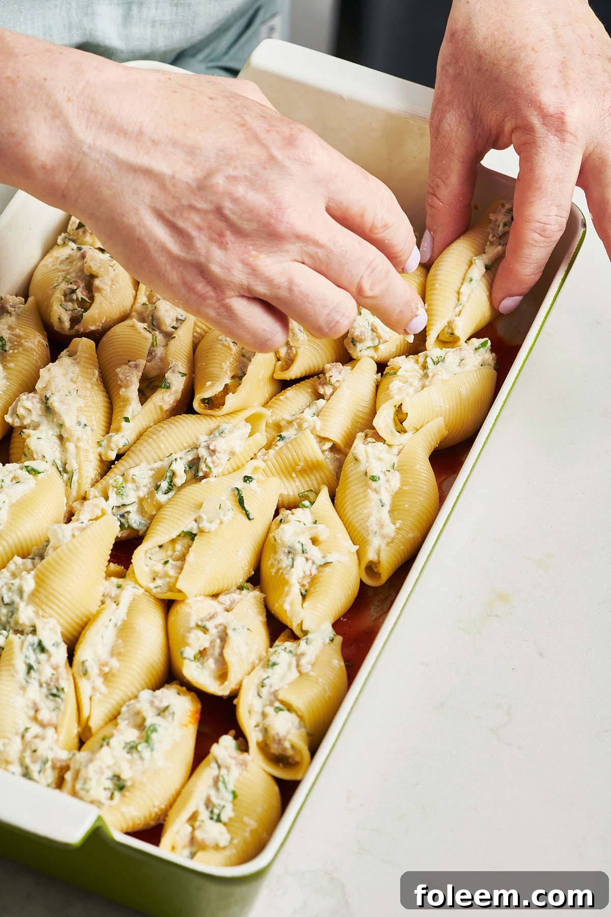 Woman arranged stuffed pasta shells in a baking dish.