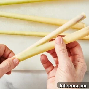Woman peeling outer layer off lemongrass stalks over cutting board.