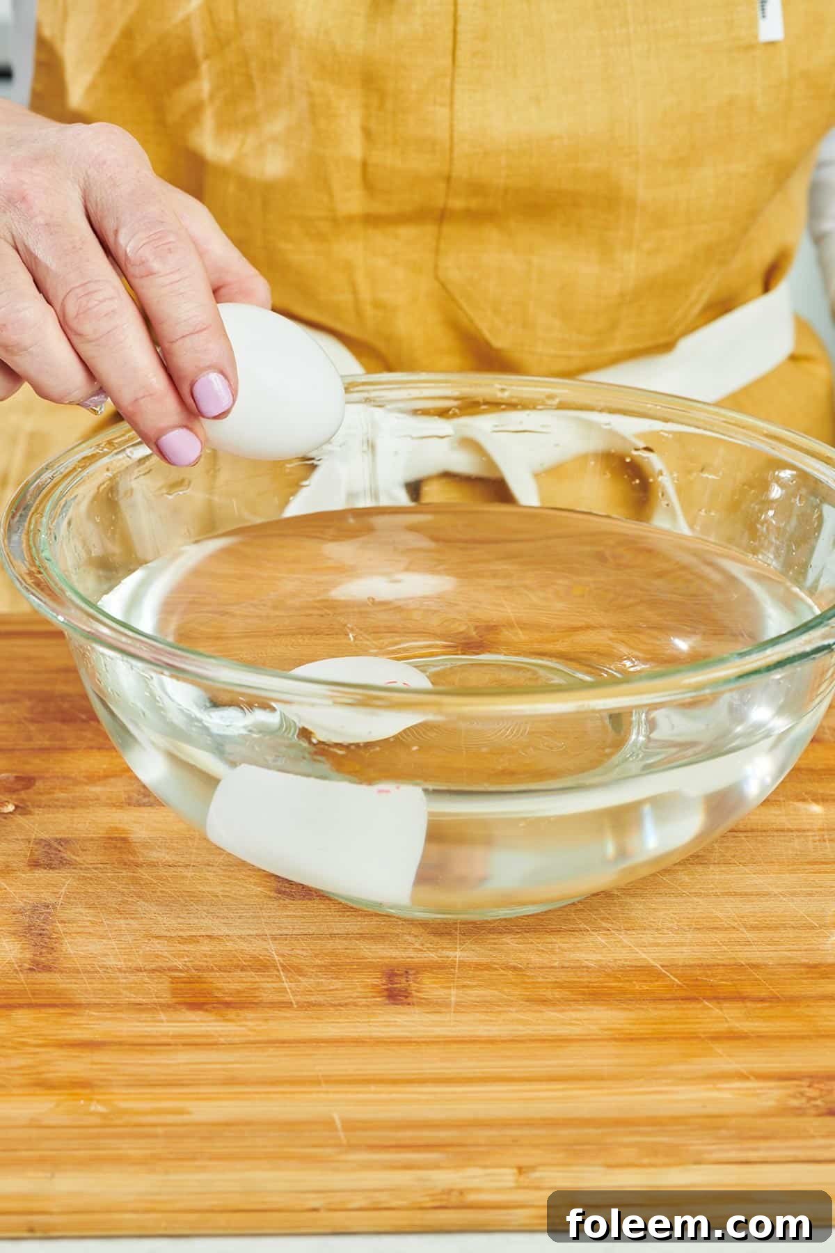Woman placing egg in glass bowl full of water.
