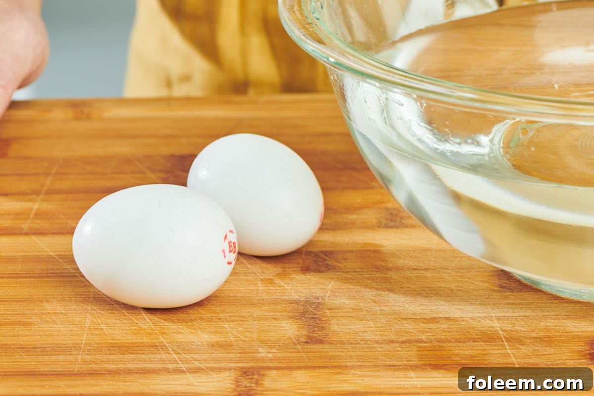 Two eggs on cutting board next to bowl of water.