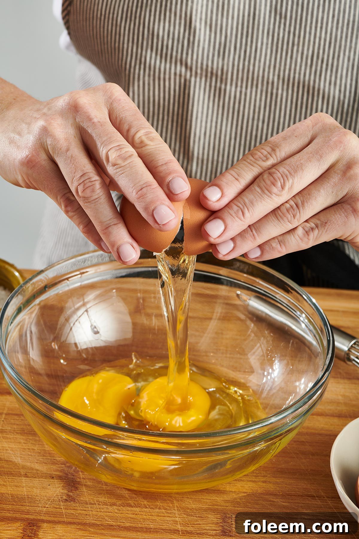Woman in apron cracking eggs in bowl.