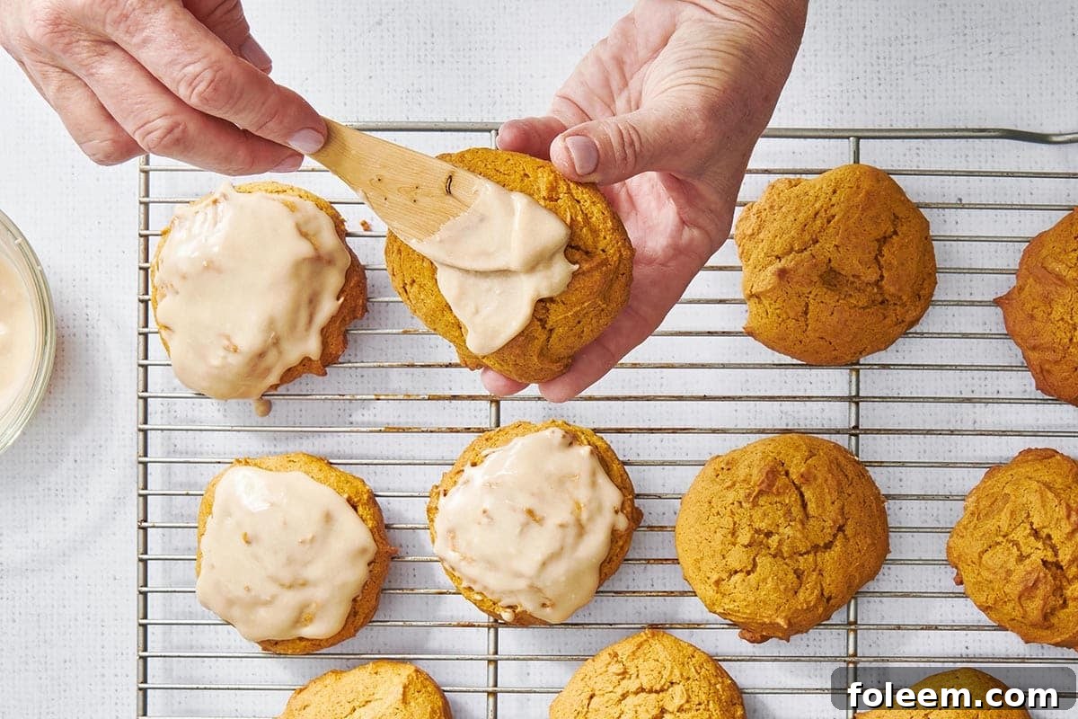 Adding icing to pumpkin cookies with kitchen spatula.