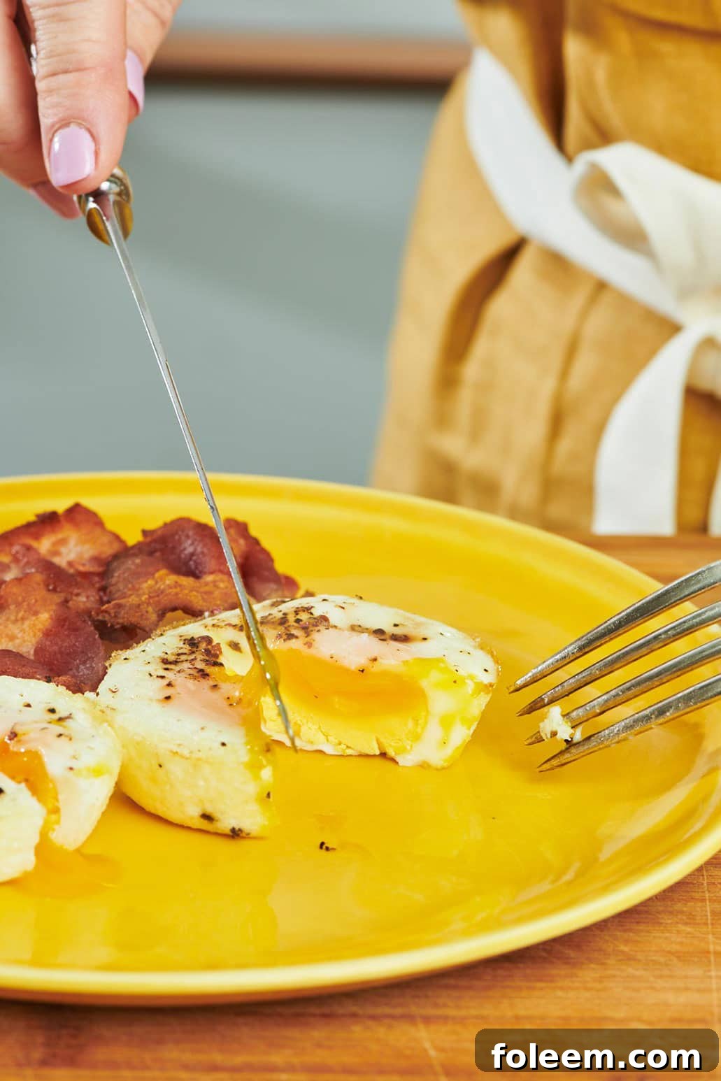 Slicing oven-baked egg with knife and fork on yellow plate.