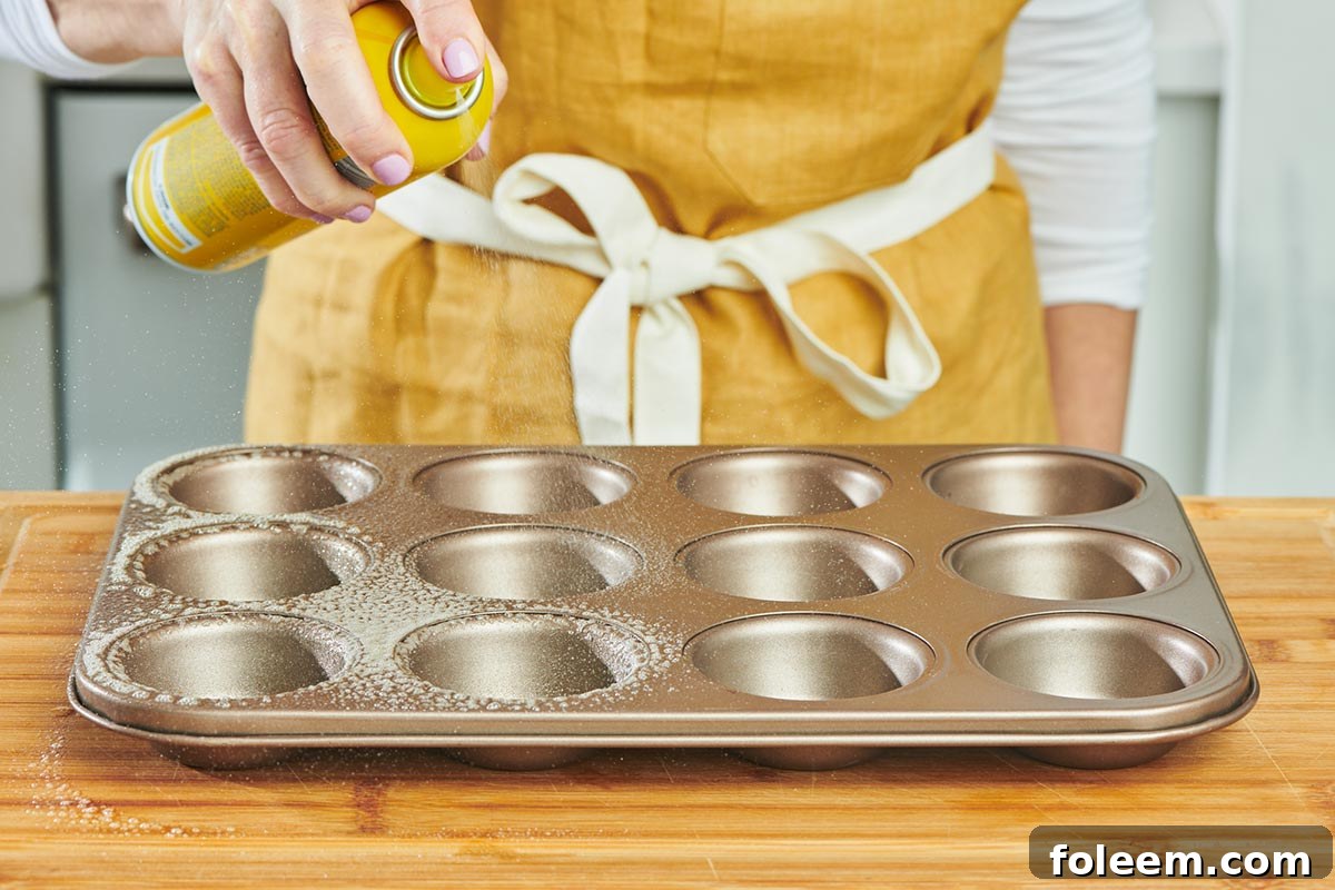 Woman spraying muffin tin with cooking spray.