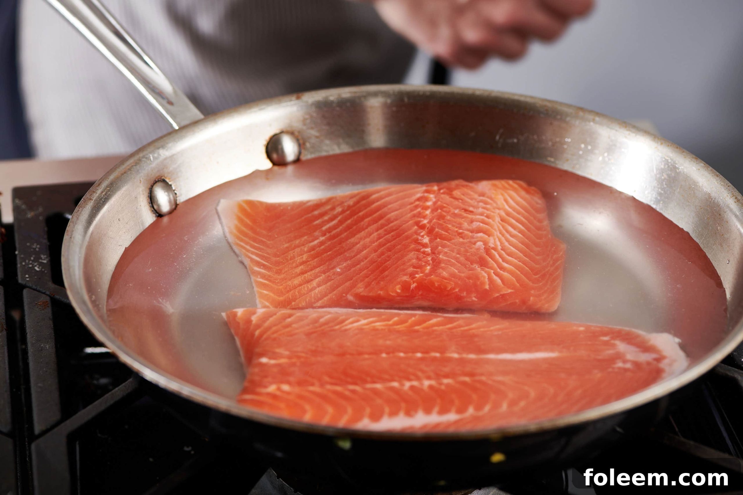 Poaching salmon filets in pan on stovetop.