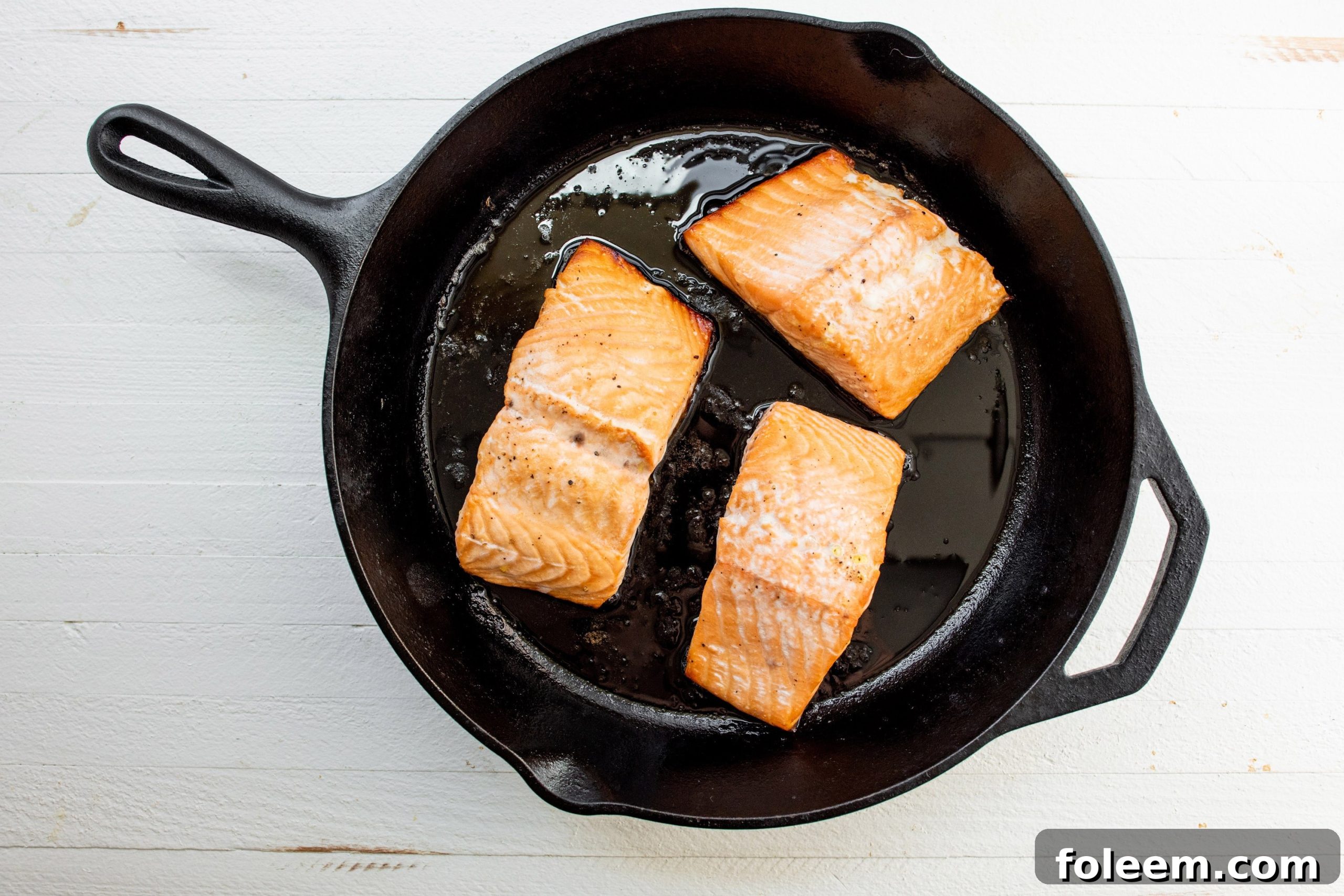 Three salmon filets in cast-iron pan.