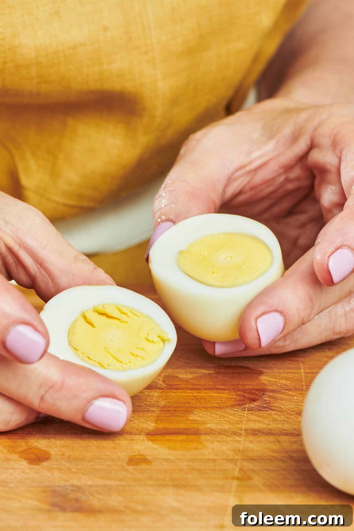 Woman holding cut hard-cooked egg on cutting board.