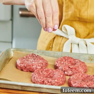 Woman sprinkling salt on raw hamburger patties.