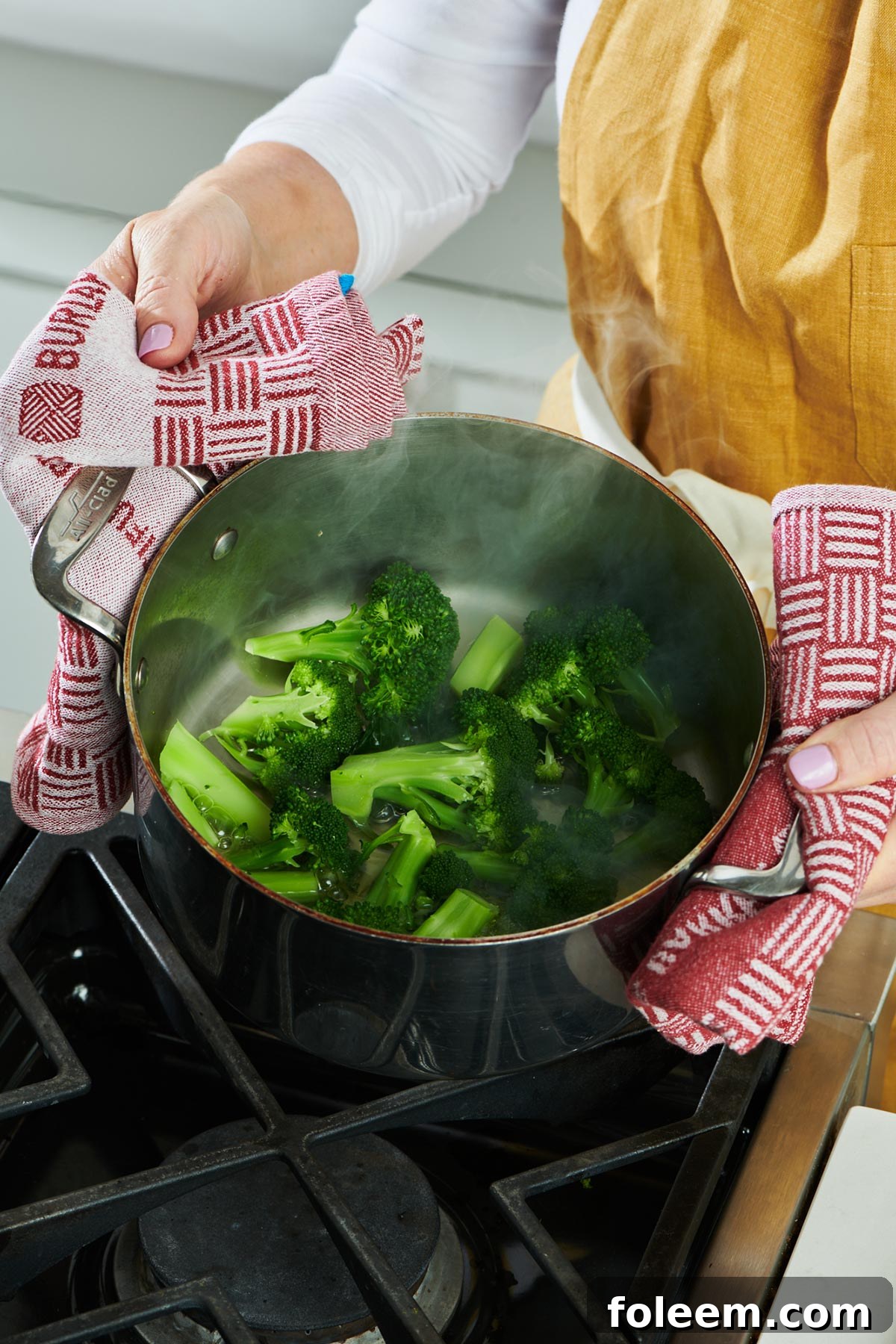 Woman holding pot of steamed broccoli over stove.