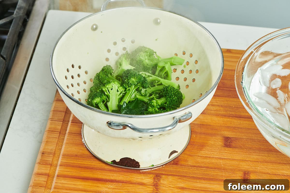 Steamed broccoli in colander on cutting board.