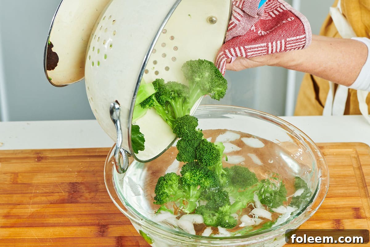 Pouring steamed broccoli into ice water bath.