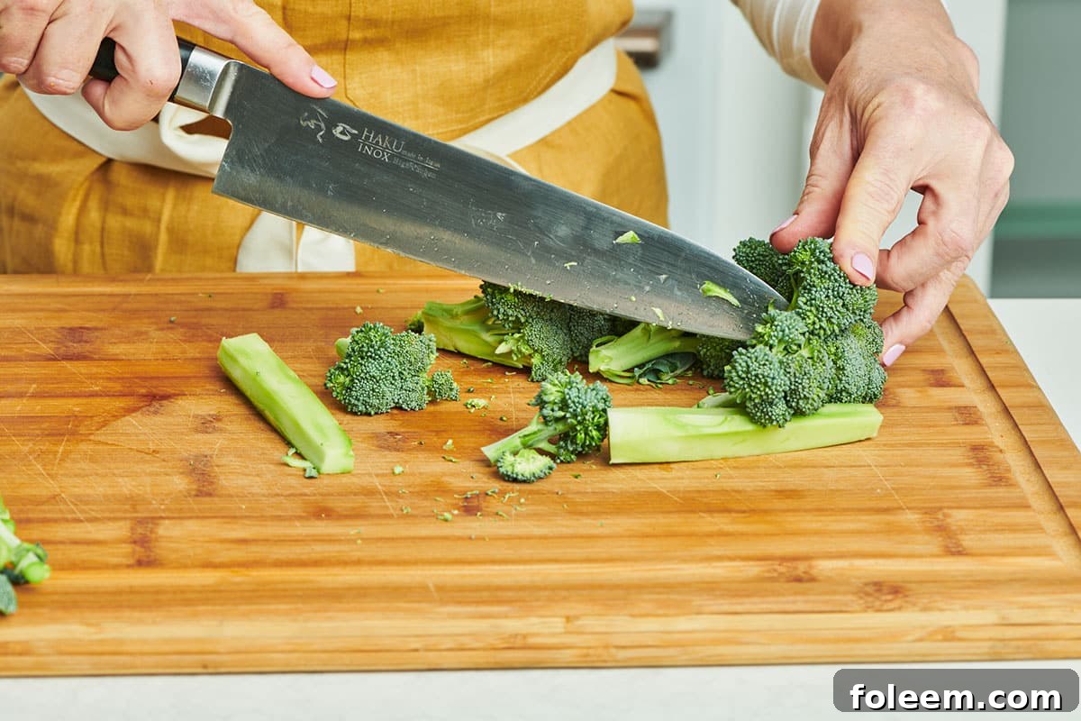 Woman cutting broccoli on wood board.