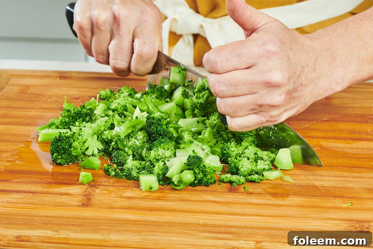 Chopping broccoli on cutting board with knife.