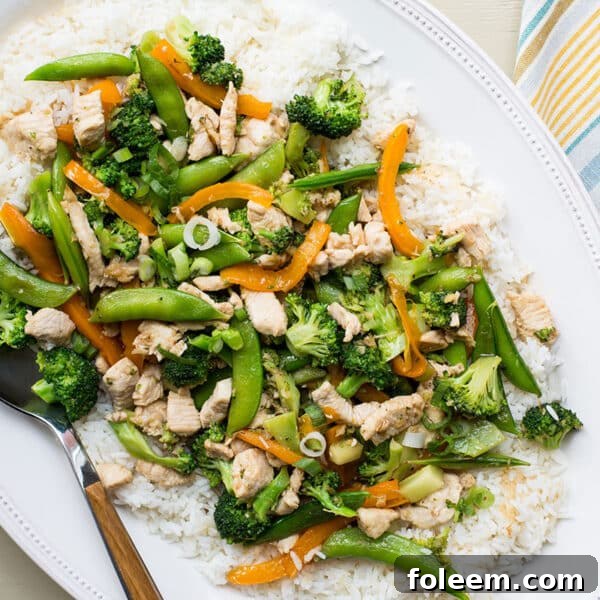 Stir-fry with chicken, broccoli, and sugar snap peas served over white rice on plate.